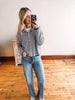 Woman taking a mirror selfie wearing a striped shirt and jeans in a room with wooden flooring.