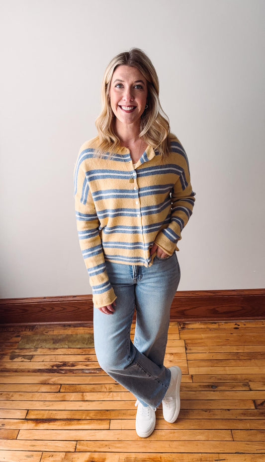 Woman wearing a striped shirt and jeans standing on a wooden floor.