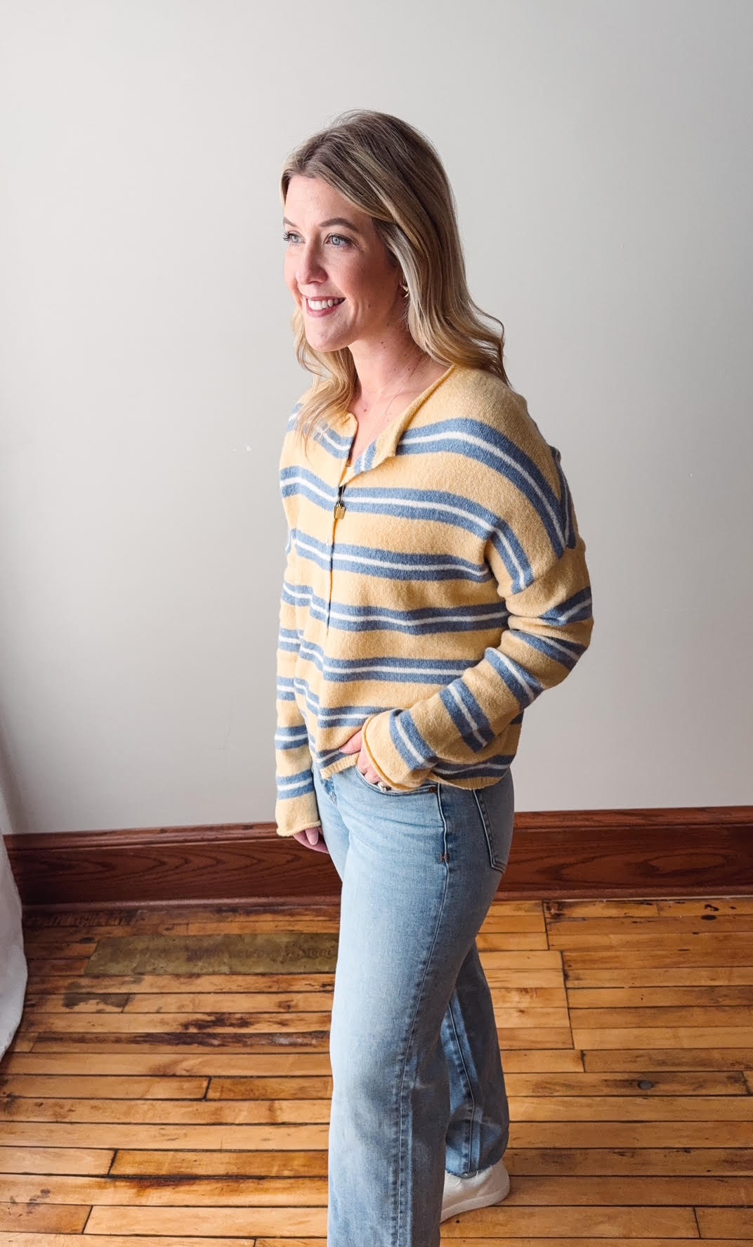 Woman wearing a striped sweater and jeans standing in a room with wooden flooring.