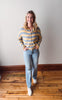 Woman wearing a striped shirt and jeans standing on a wooden floor.