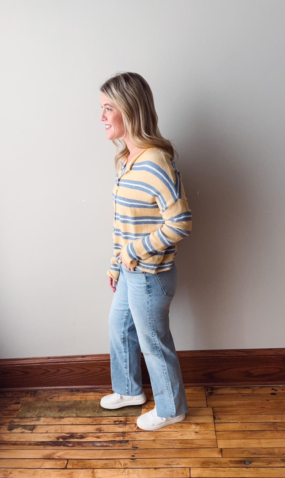 Woman wearing a striped sweater and jeans standing against a plain wall.