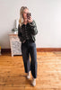 Woman taking a mirror selfie wearing a dark green shirt and black jeans in a room with wooden flooring.