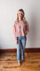 Woman wearing a pink floral blouse and blue jeans standing on a wooden floor.