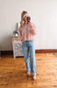 Woman taking a mirror selfie wearing a pink floral blouse and blue jeans in a room with wooden flooring.