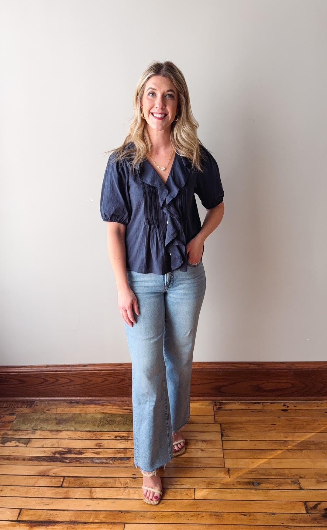 Woman wearing a navy blouse and light blue jeans standing on a wooden floor.