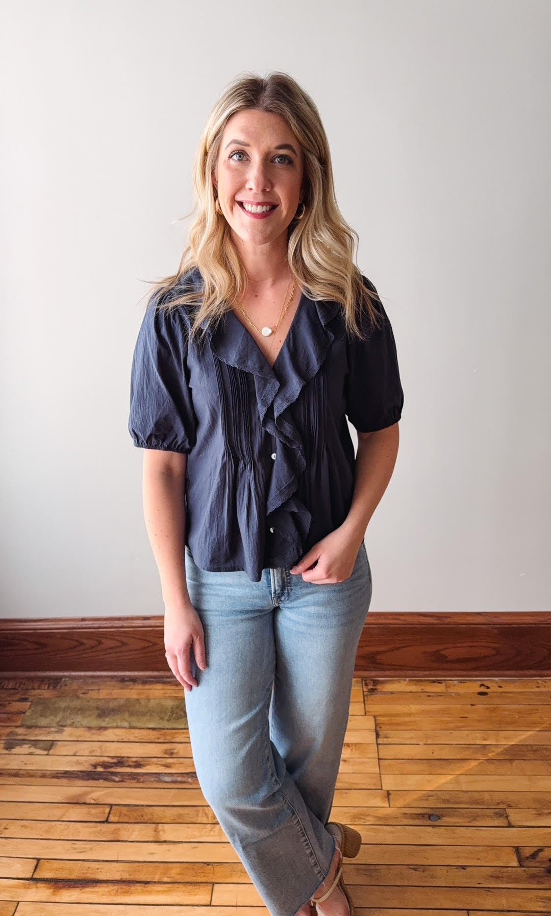 Woman wearing a navy blue blouse and light blue jeans standing on a wooden floor.