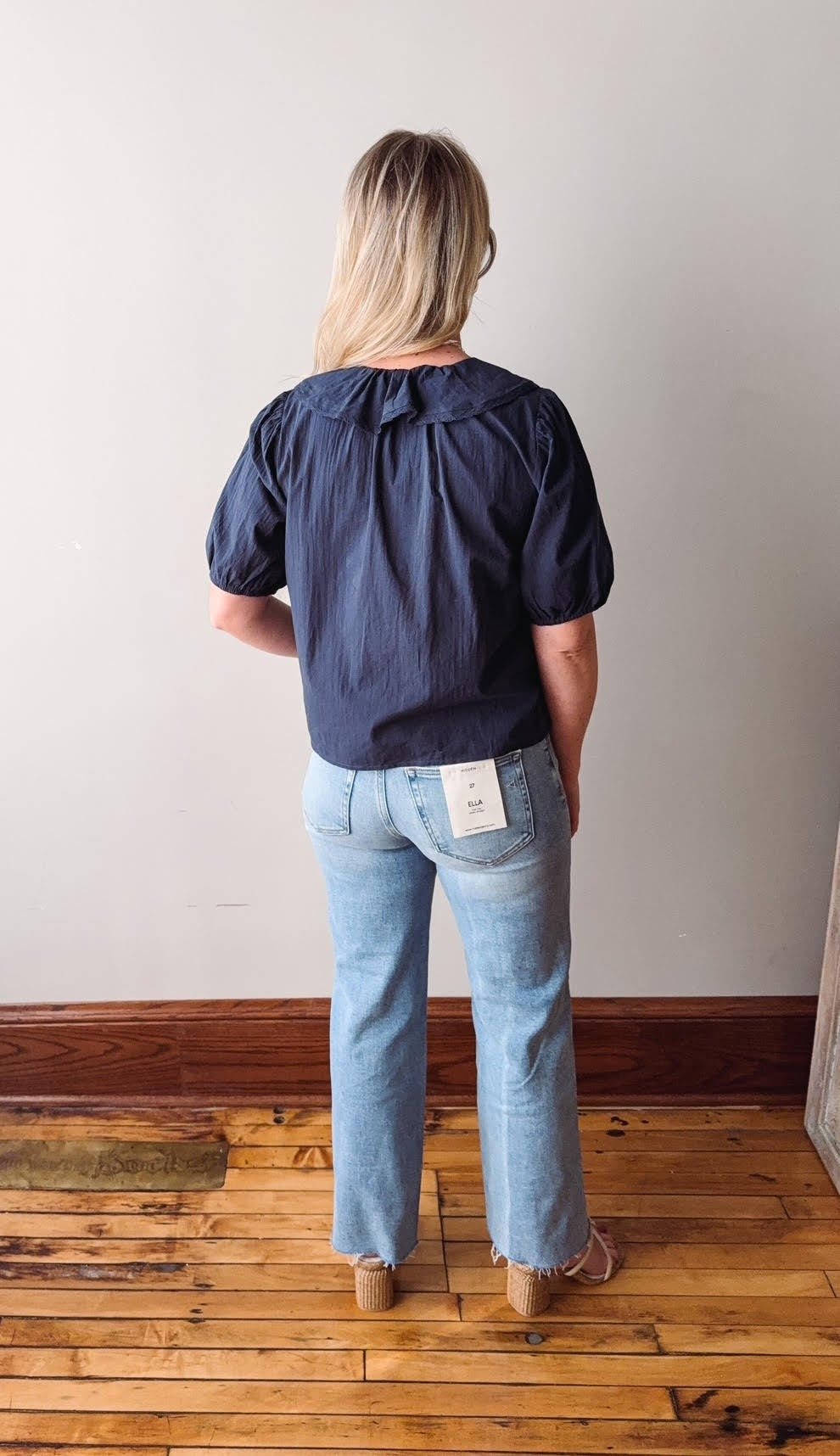 Person wearing a navy blouse and light blue jeans standing on a wooden floor.