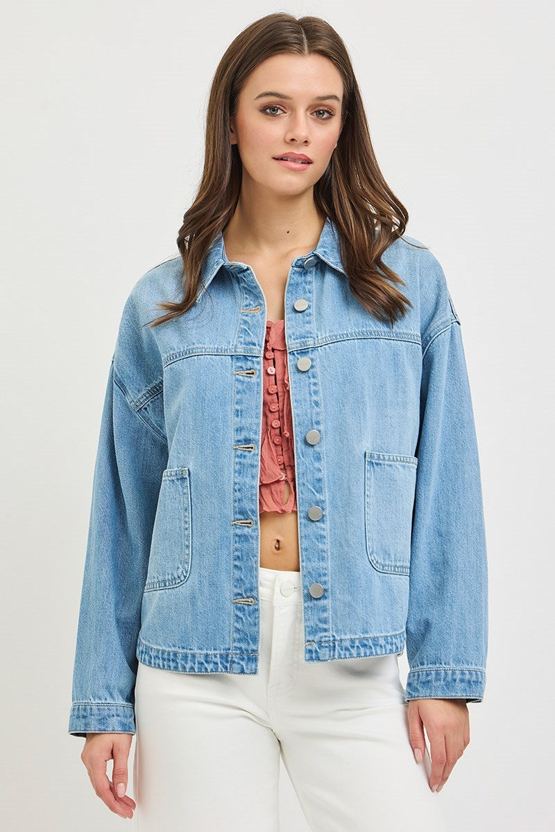 Woman wearing a light blue denim jacket over a pink top on a white background