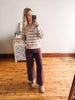 Woman taking a mirror selfie wearing a striped sweater and burgundy pants in a room with wooden flooring.