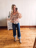 Woman taking a mirror selfie wearing a floral blouse and blue jeans in a room with wooden flooring.