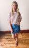 A woman wearing a red and white striped pocket tee with a blue denim skirt and beige sandals.