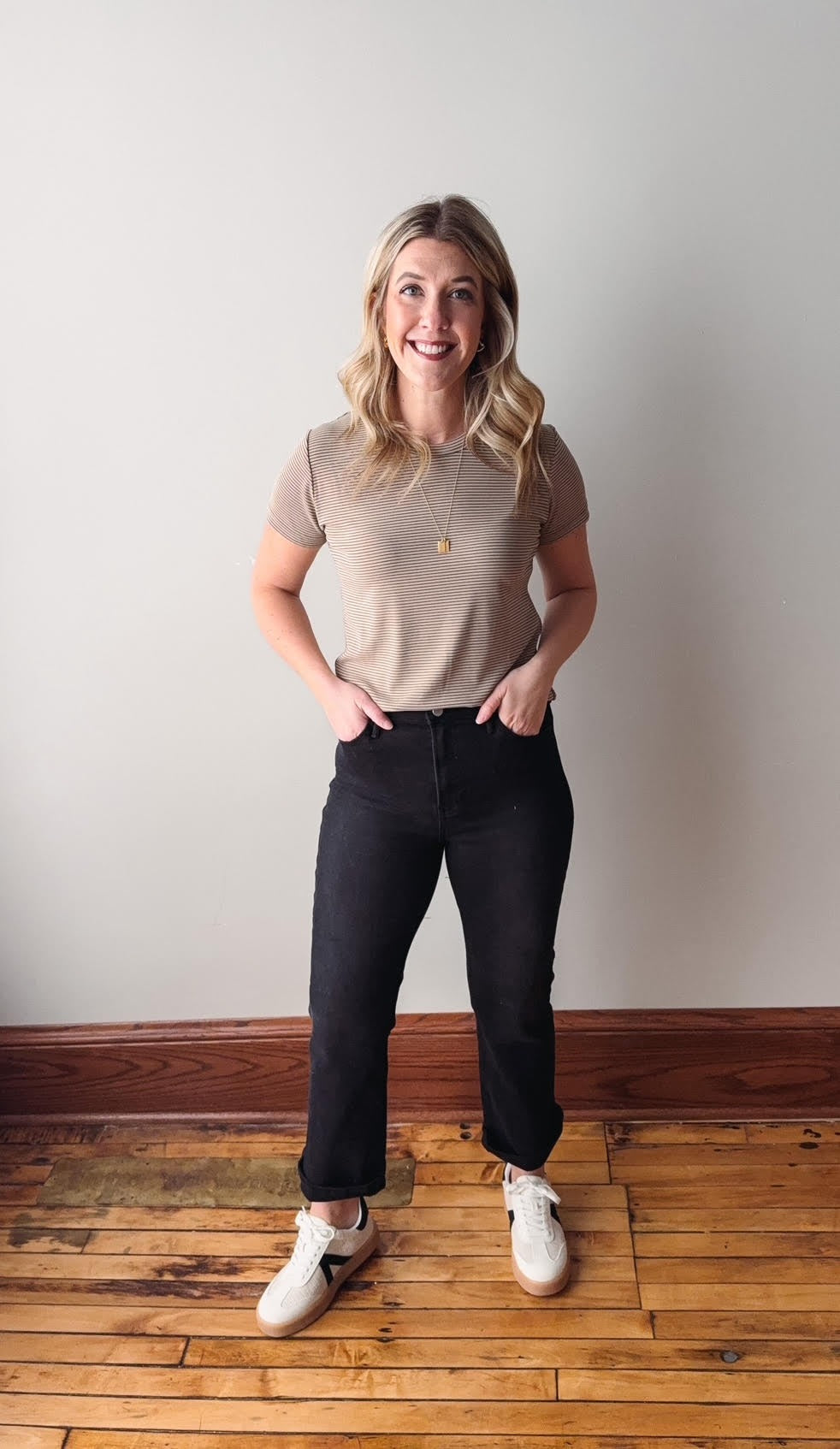 Woman standing on a wooden floor wearing a beige top and black pants.