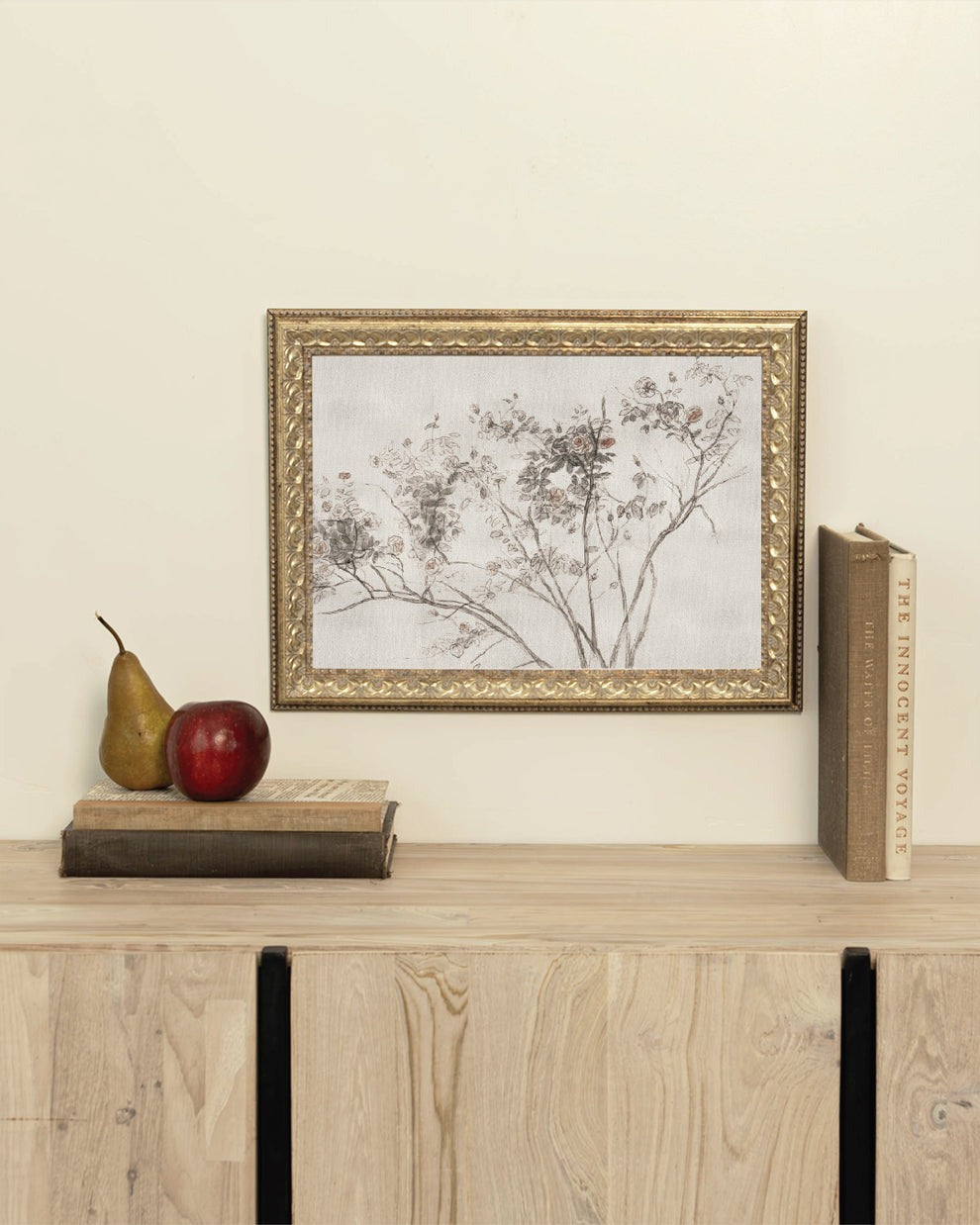 Framed artwork on a wooden shelf with books and a pear