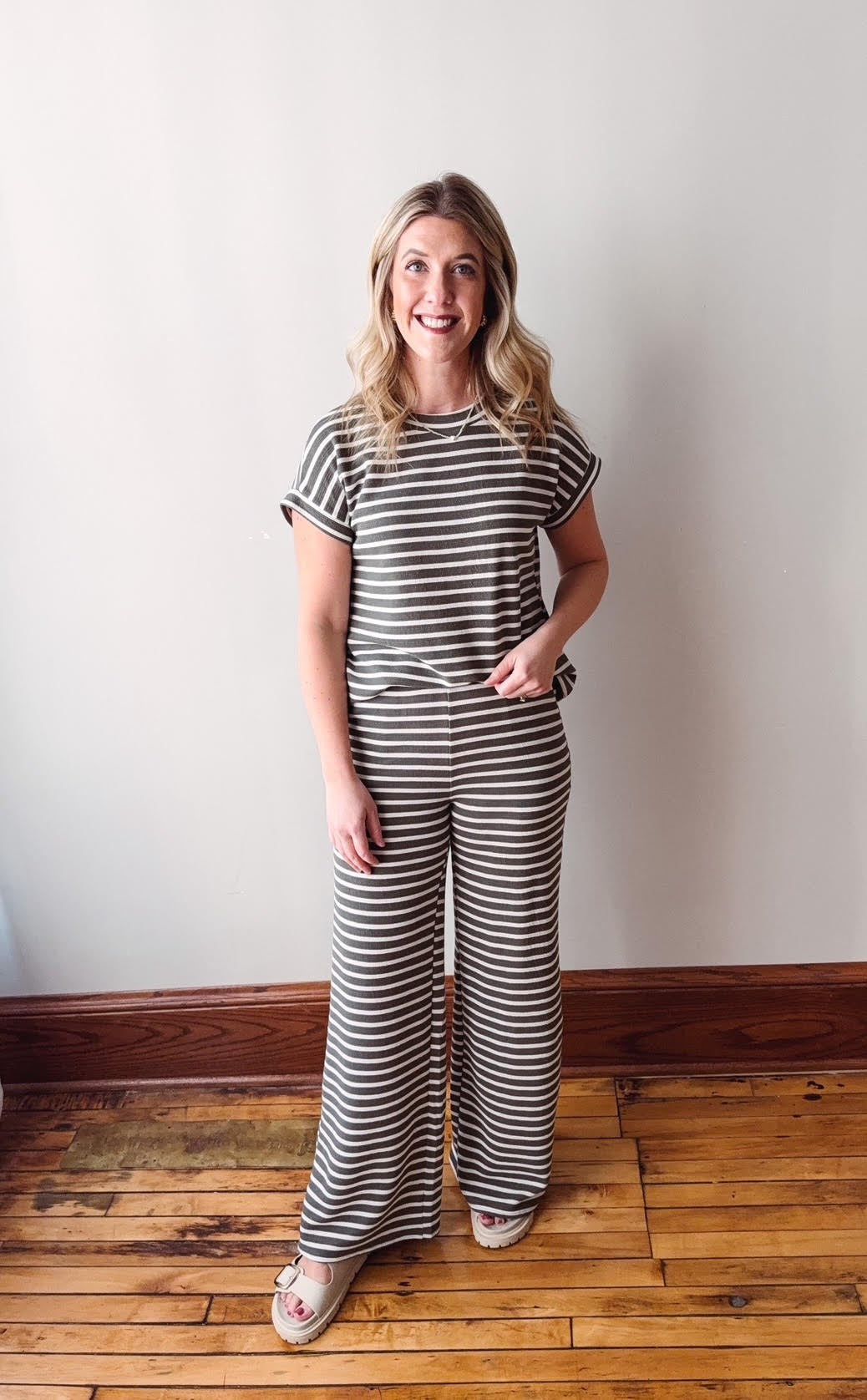 Woman wearing a black and white striped outfit standing on a wooden floor with a white wall background