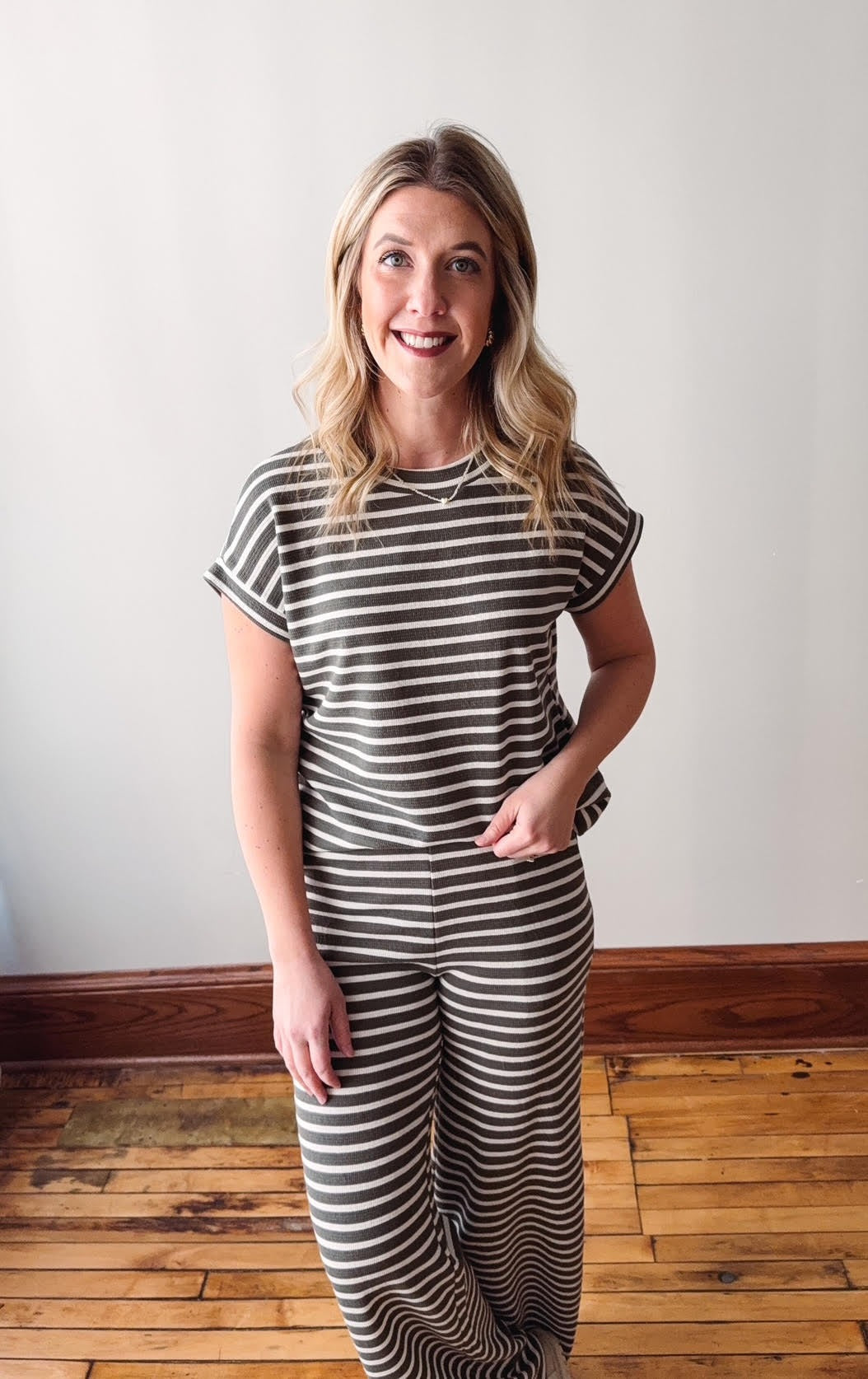 Woman wearing a striped outfit standing on a wooden floor with a white wall background