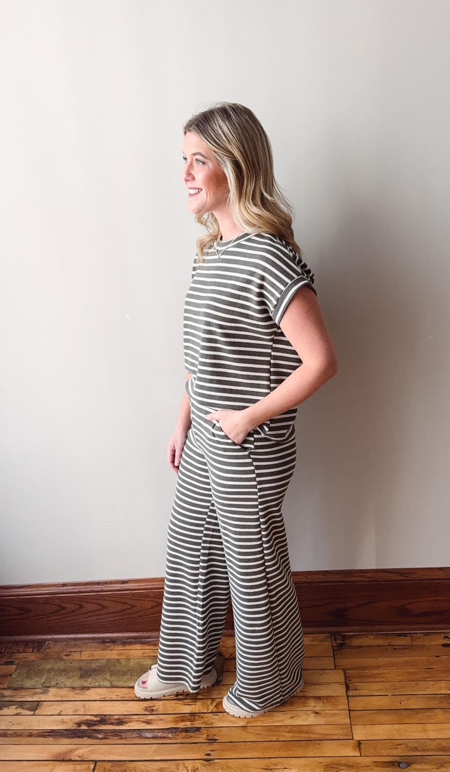 Woman wearing a black and white striped outfit standing against a plain wall.