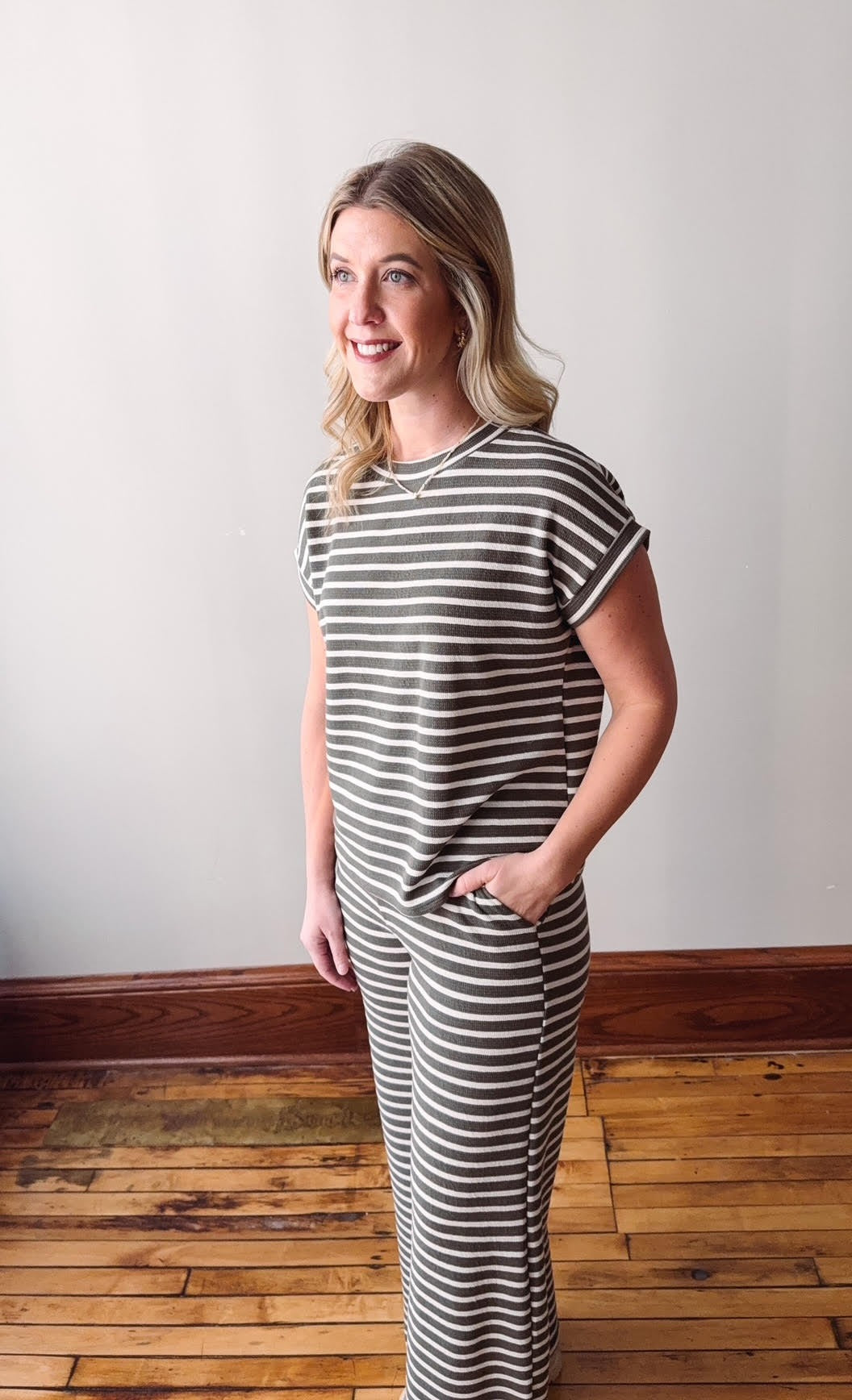 Woman wearing a striped dress standing on a wooden floor with a white wall background