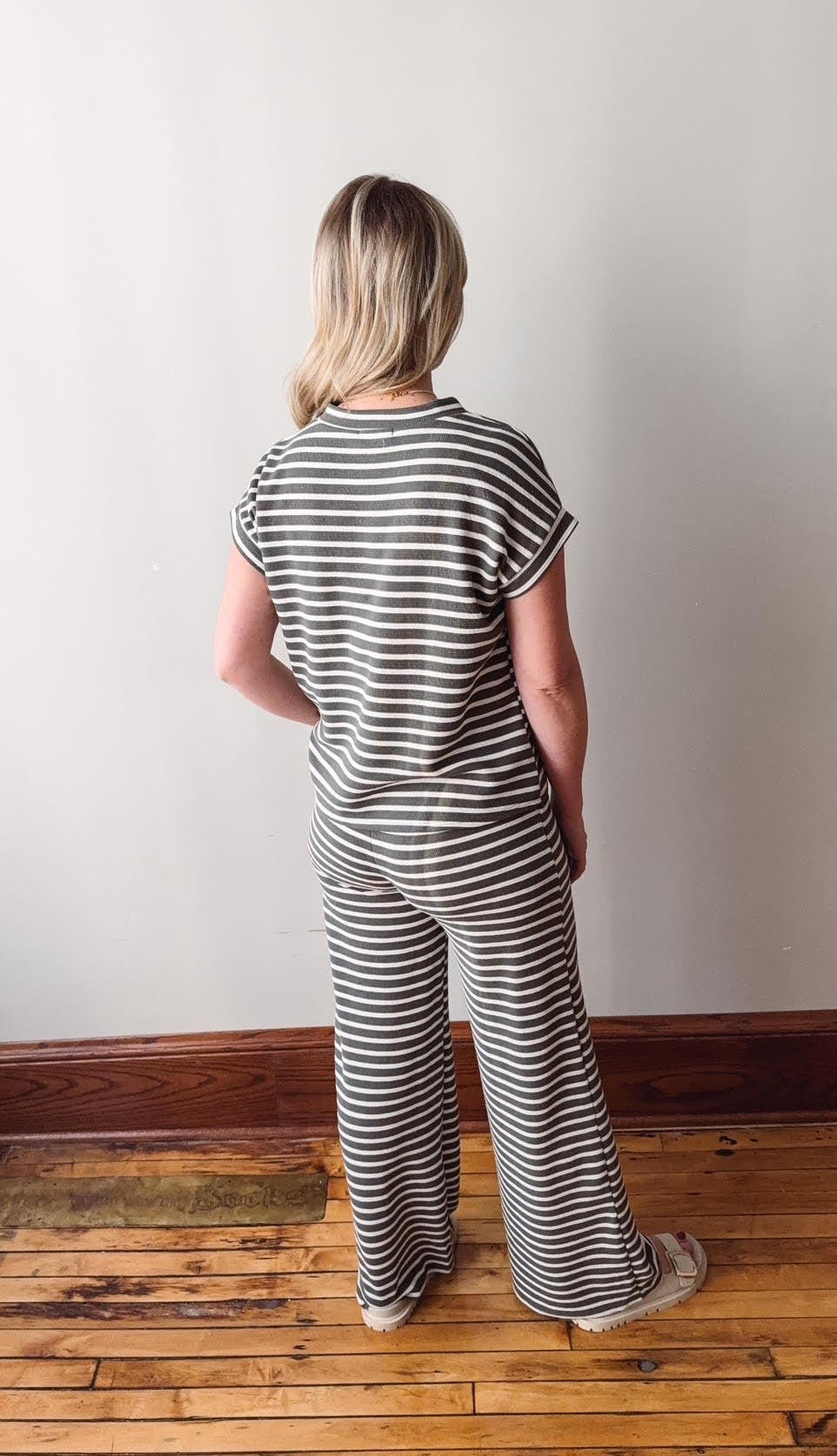 Person wearing a black and white striped outfit standing on a wooden floor with a white wall background