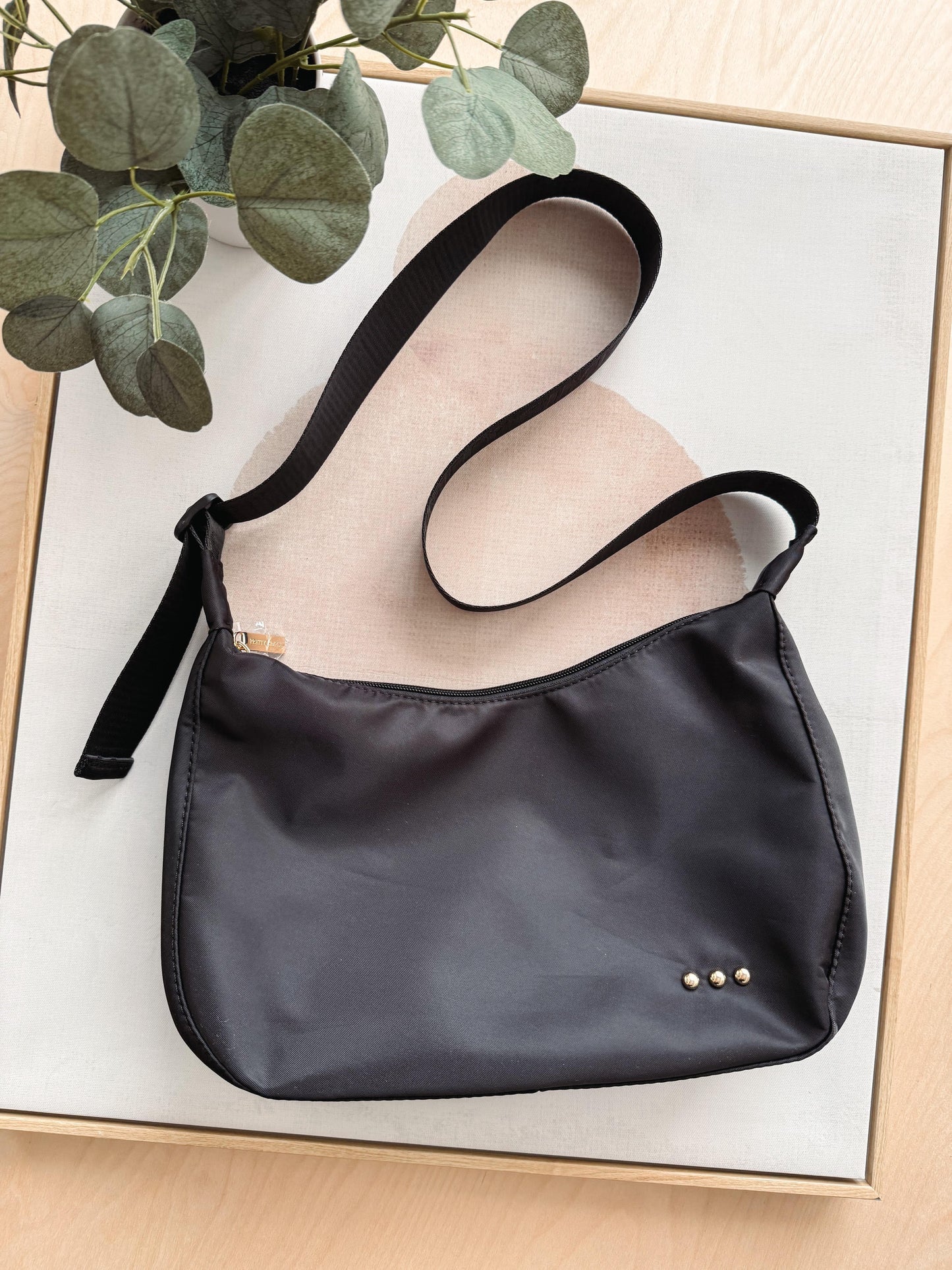 Black handbag on a light wooden surface with a plant in the corner