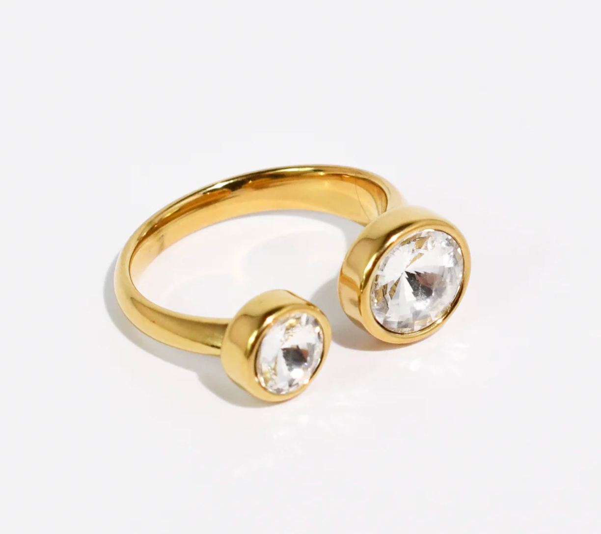 Gold ring with two clear gemstones on a light gray background