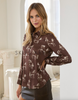 A woman modeling a brown long-sleeve button-up blouse with a white horse print, paired with a dark gray skirt, in a bright, classical-style interior setting.