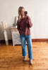 Woman taking a mirror selfie wearing a maroon sweater and blue jeans in a room with wooden flooring.