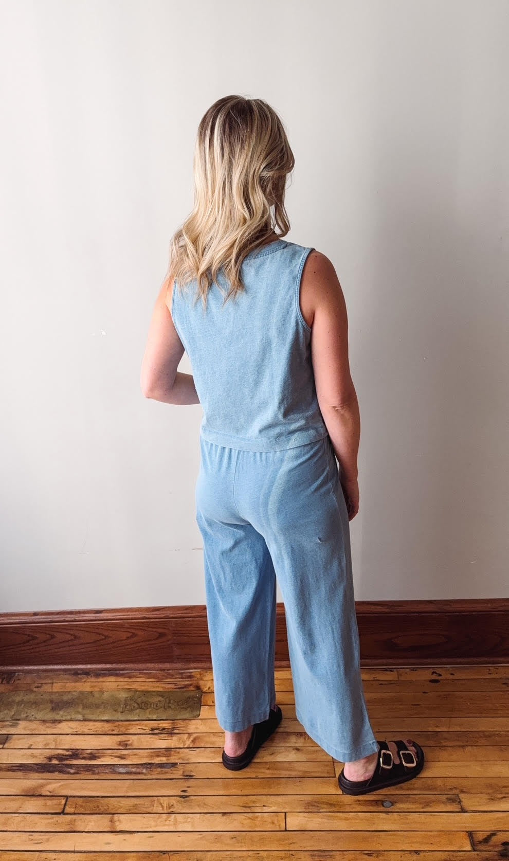 Woman wearing a light blue jumpsuit standing against a plain wall.
