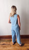Woman wearing a light blue jumpsuit standing against a plain wall.
