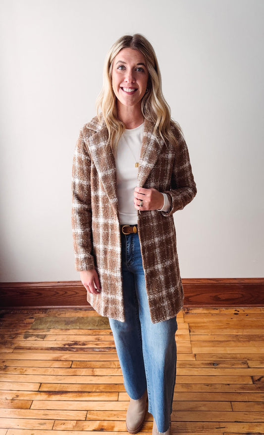 Woman wearing a plaid coat over a white shirt and blue jeans on a wooden floor.