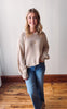 Woman wearing a beige sweater and blue jeans standing in a room with wooden flooring.