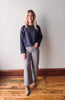 Woman wearing a navy sweater and gray pants standing against a plain wall.