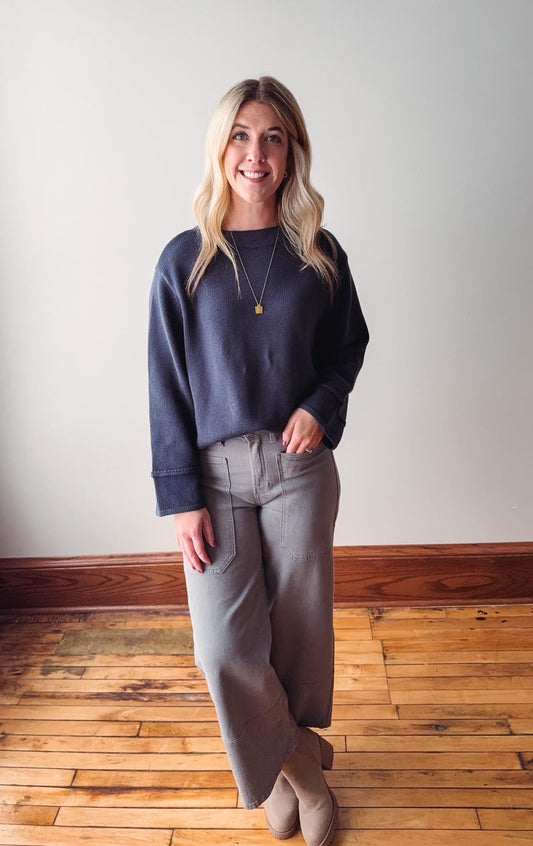 Woman wearing a navy sweater and gray pants standing on a wooden floor.