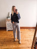 Woman taking a mirror selfie wearing a navy sweater and light gray jeans in a room with wooden flooring.