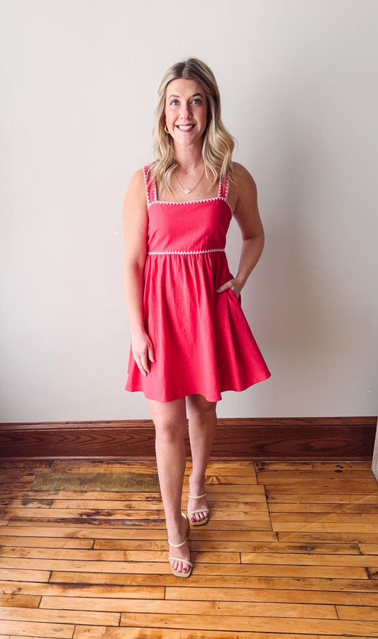 Woman wearing a red dress standing on a wooden floor with a white wall background