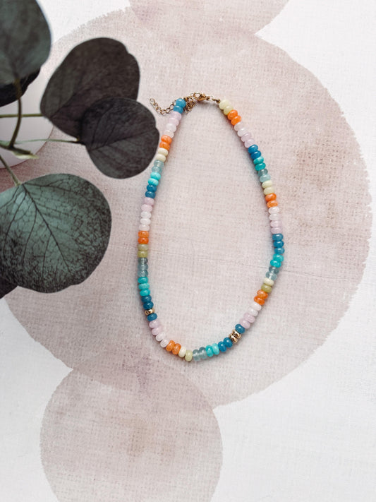 Colorful beaded necklace on a textured surface with leaves in the background