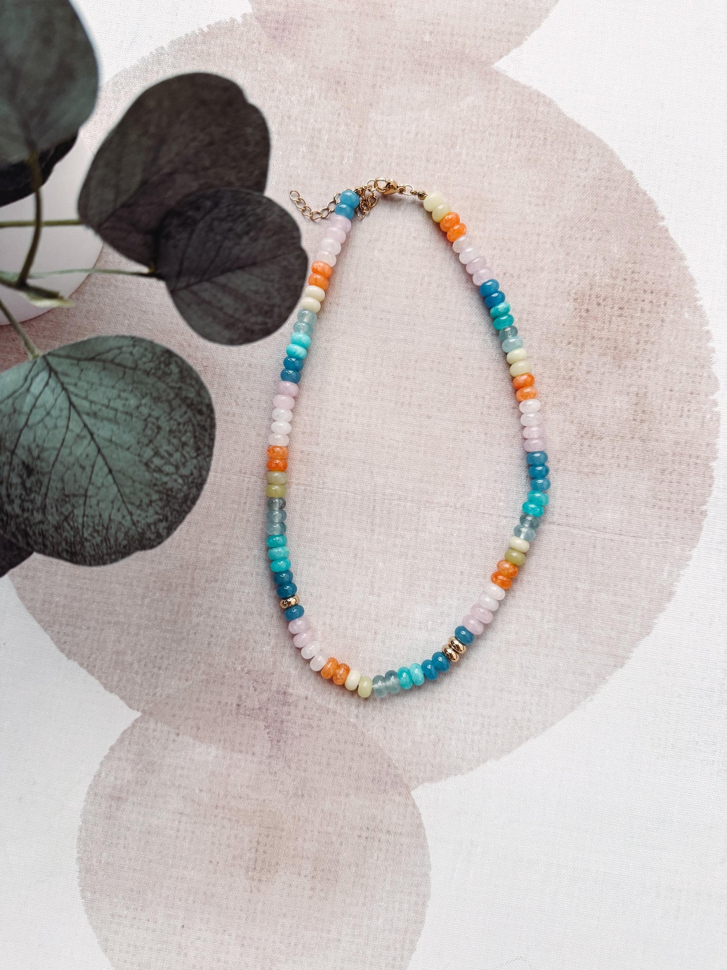 Colorful beaded necklace on a textured surface with leaves in the background