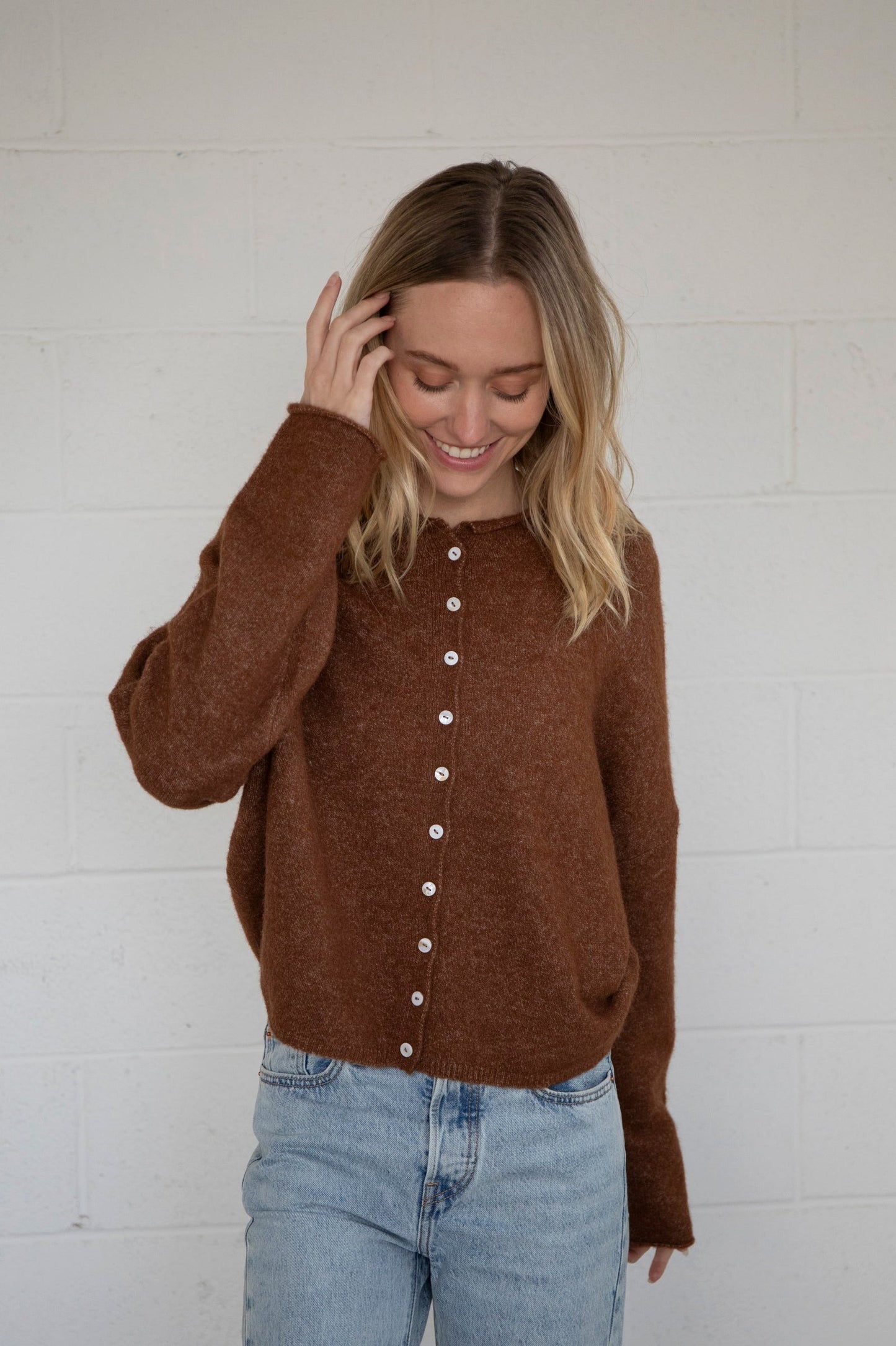 Woman wearing a brown sweater with white buttons against a white wall