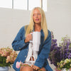 Woman holding a mug with flowers in the foreground and a white wall in the background