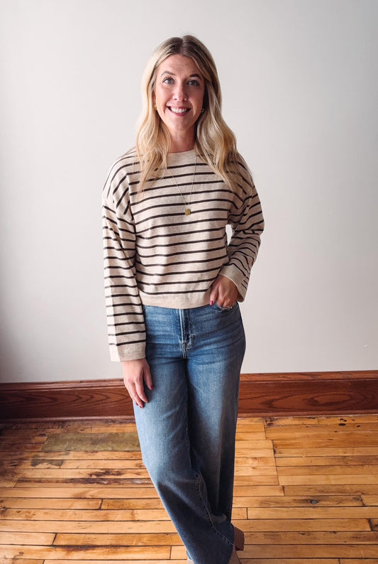 Woman wearing a striped sweater and jeans standing on a wooden floor.