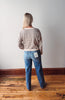 Person wearing a striped sweater and blue jeans standing on a wooden floor with a white wall background