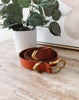 Brown leather belt with gold buckle on a wooden surface with a plant in the background
