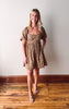 Woman wearing a patterned dress standing on a wooden floor against a white wall