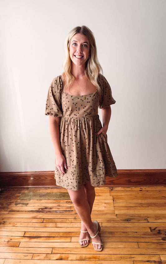 Woman wearing a patterned dress standing on a wooden floor with a white wall background