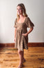 Woman wearing a patterned dress standing on a wooden floor with a white wall background