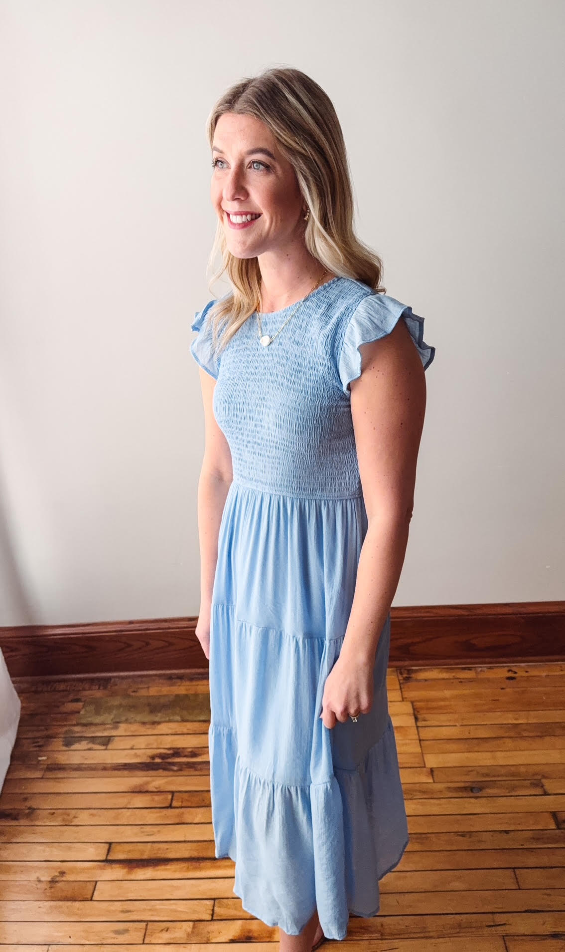 Woman wearing a light blue dress with ruffled sleeves in a room with wooden flooring.