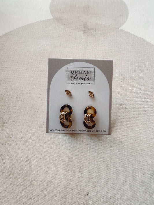 Pair of gold earrings on a card with 'Urban Threads' branding against a beige background