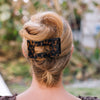 Person with a styled bun holding a leopard print hair clip outdoors