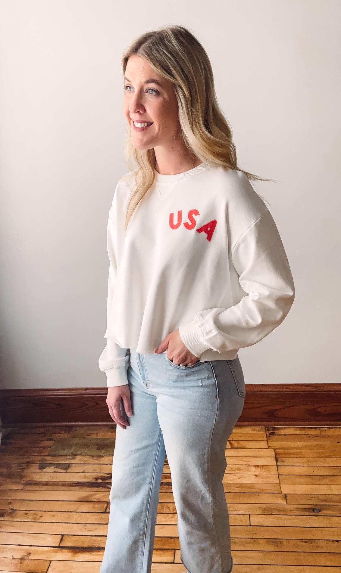Woman wearing a white shirt with 'USA' text standing indoors.
