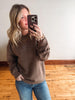 Woman taking a mirror selfie wearing a brown sweatshirt and blue jeans.