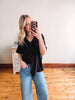 Woman taking a mirror selfie wearing a black shirt and blue jeans in a room with wooden flooring.